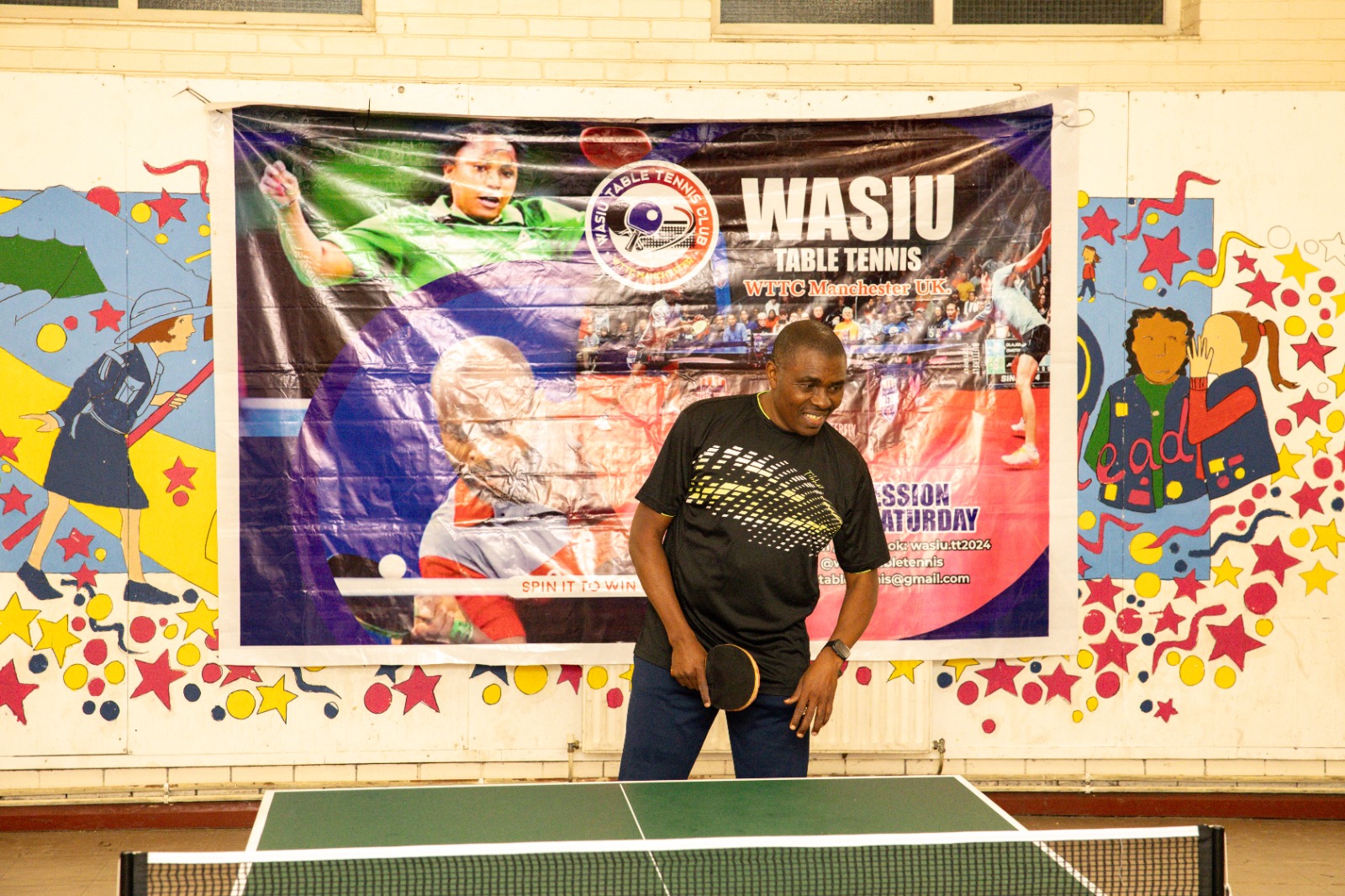 Wasiu smiling at the table in front of the club banner