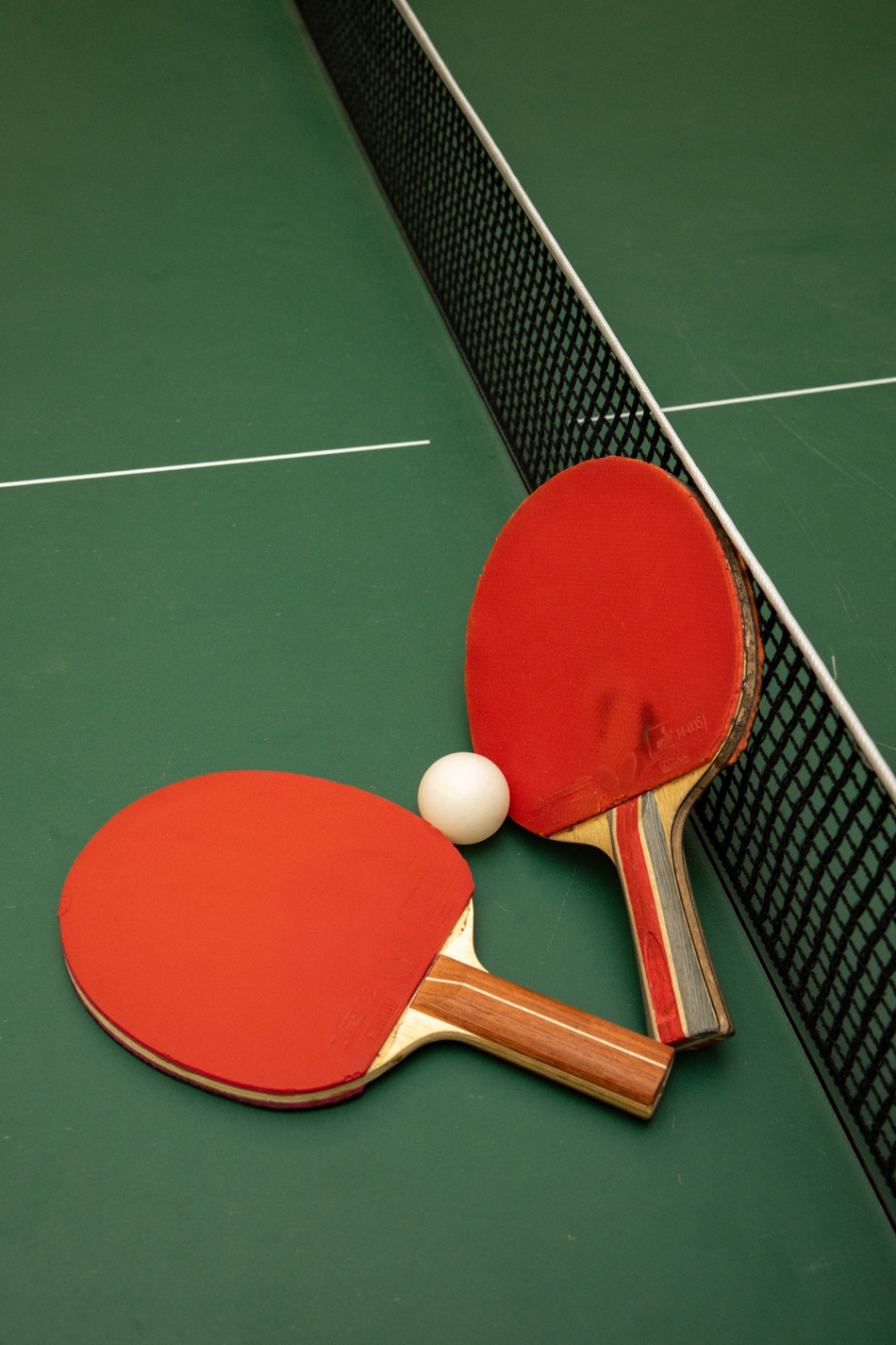 Two red table tennis bats and a ball on a green table